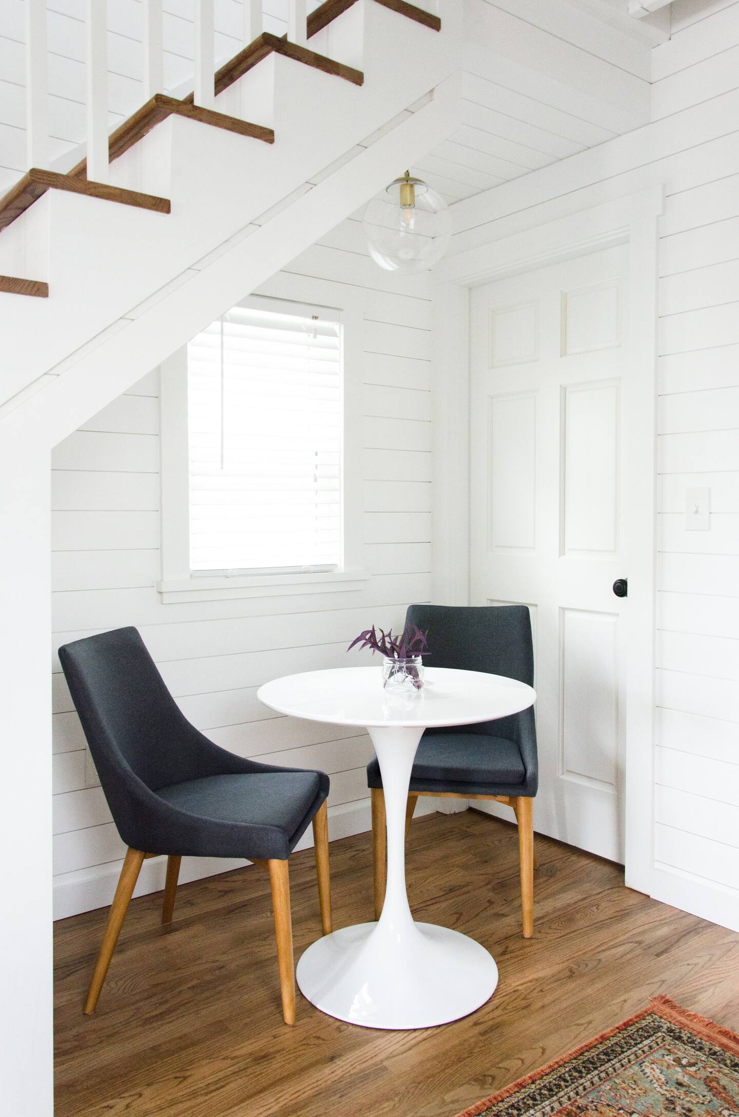 Dining room below the stairs with white round table and two gray chairs