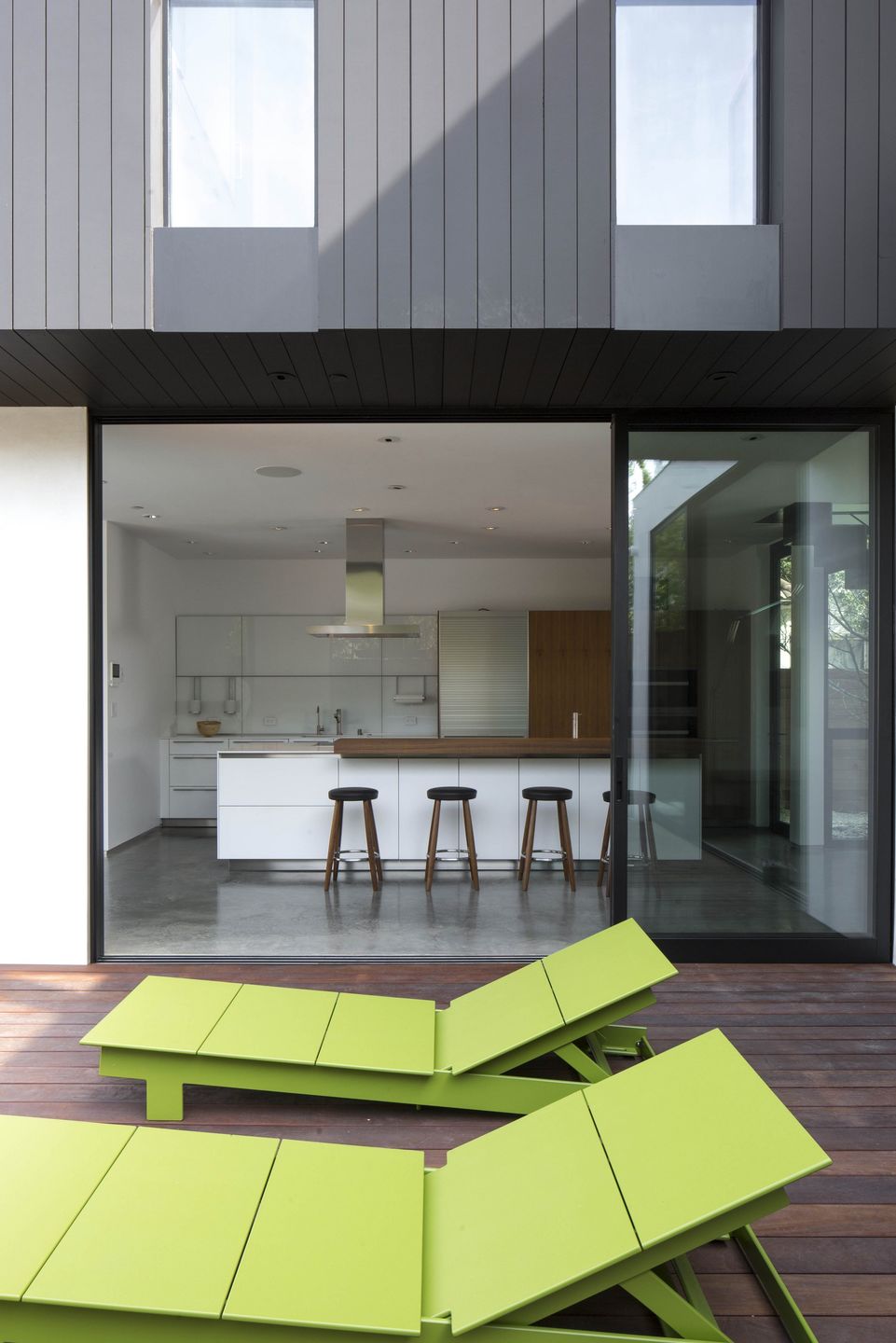 Two green chairs on a terrace and the kitchen behind