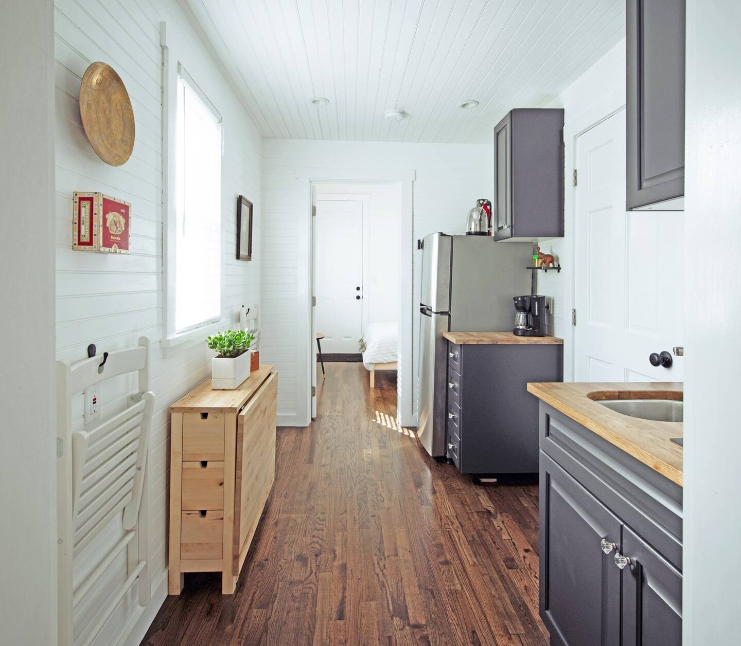 Gray tiny kitchen with a coffee maker in the corner and a wooden board