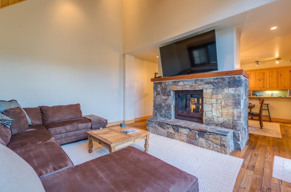 Huge fireplace made of stone in the middle of the room with TV above it, and large brown sofa