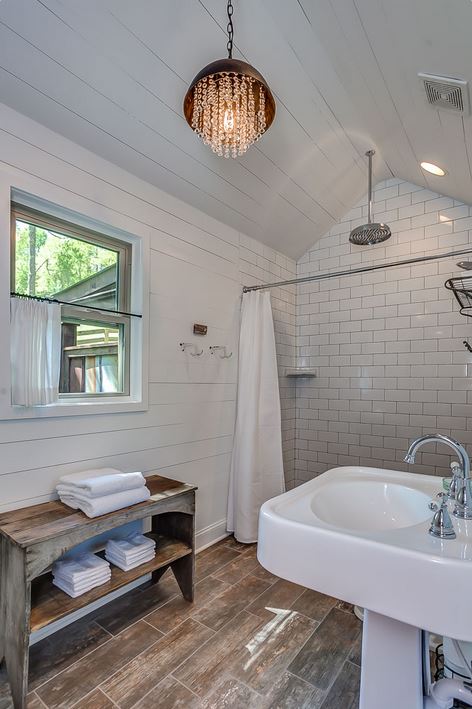 bathroom of a rustic cbain, wooden floor and shelf, white walls, big shower with white tiles