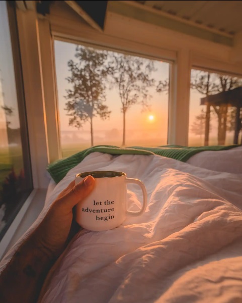 Person holding a coffee mug in bed during sunrise