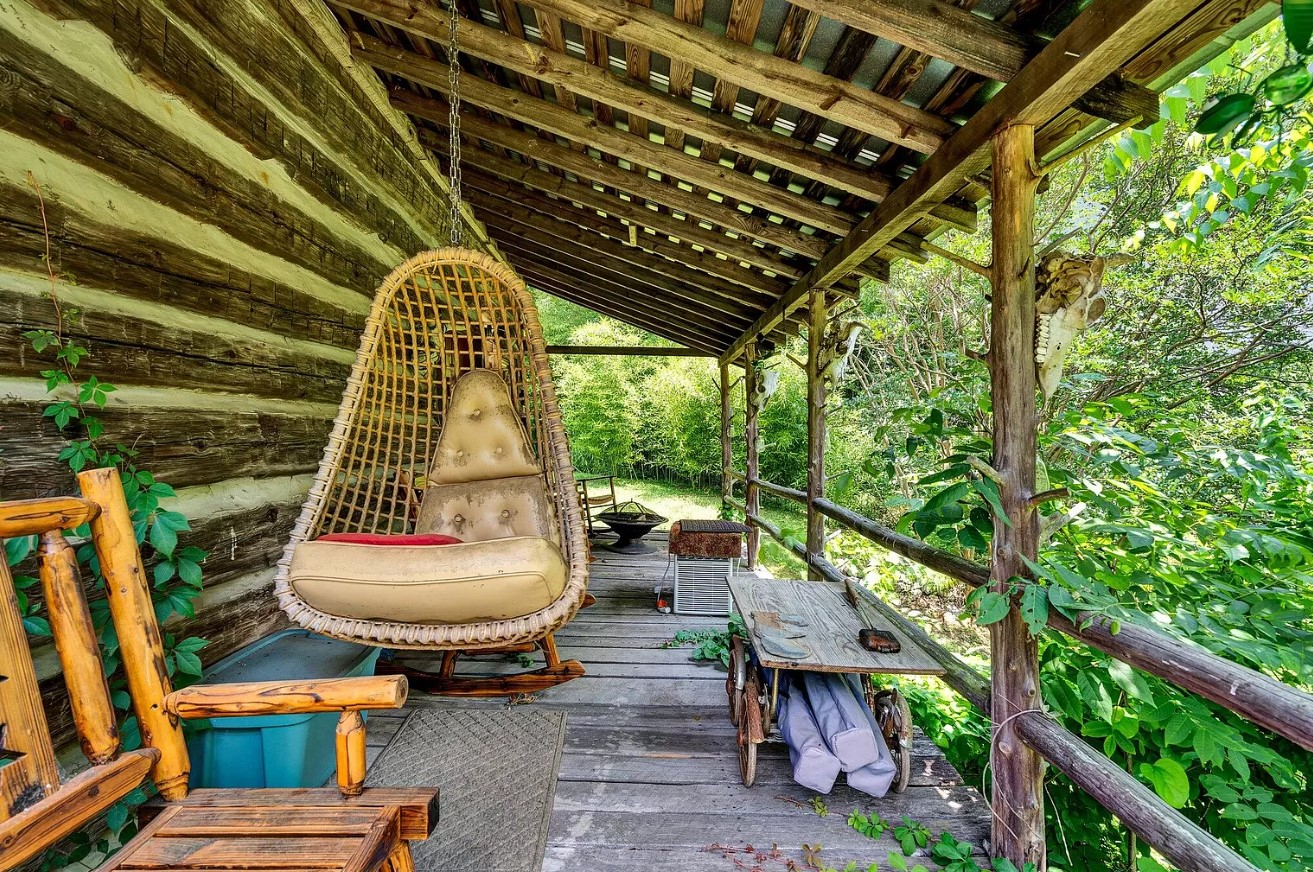 porch of an old cabin with a hanging chair, in the woods