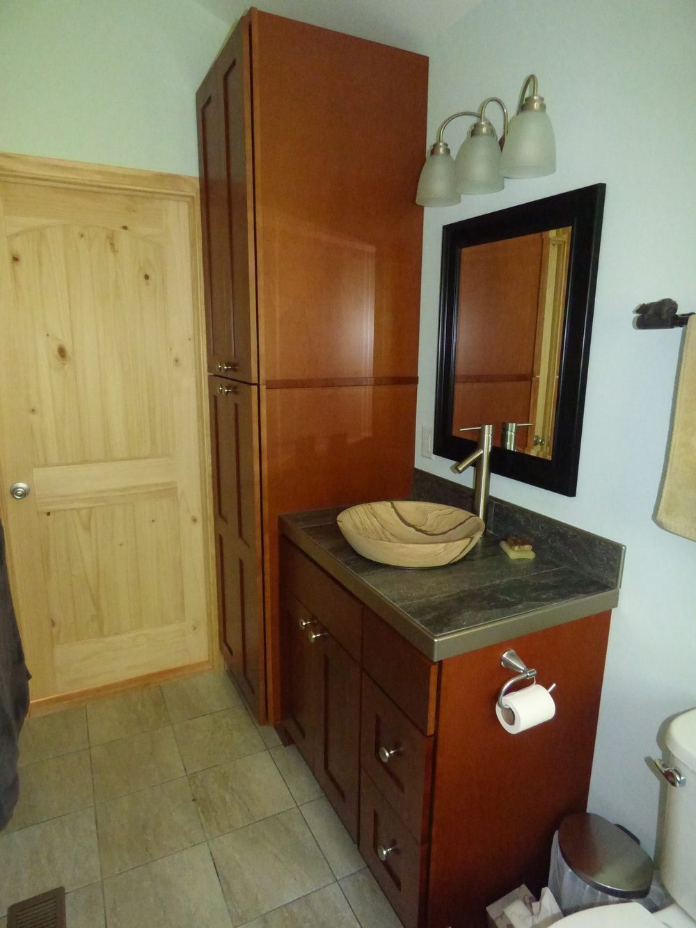 Bathroom with a ceramic sink which looks like a wooden one, and dark brown cabinets in toillette