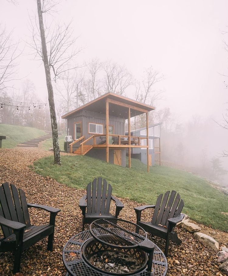 Container home in fog, with a three black chairs and a fireplace in front of it