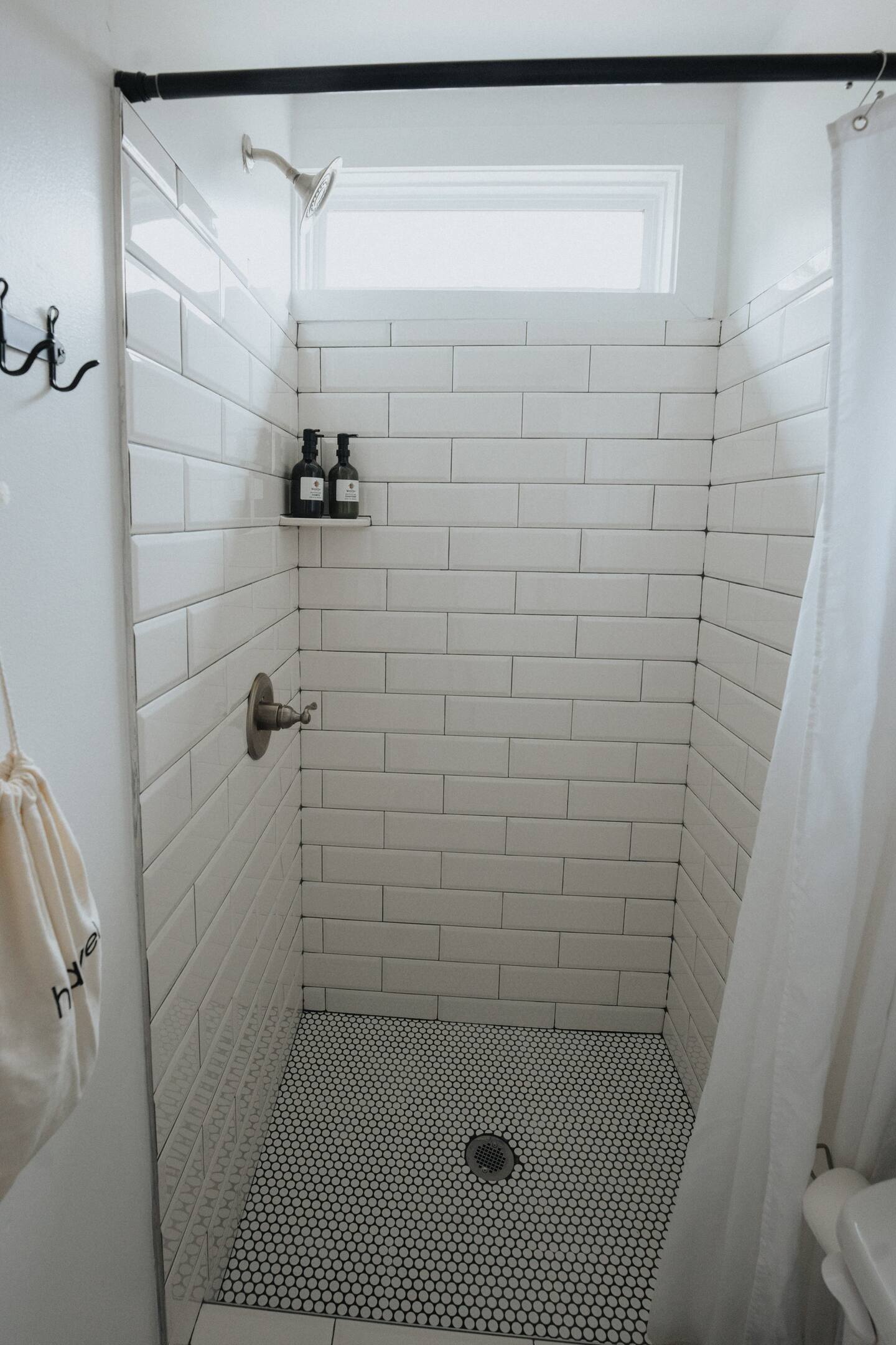 Shiny shower with black and white tiles on the floor and white shower curtain