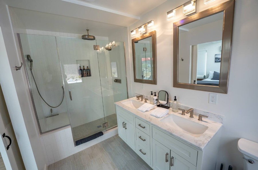 bathroom with a big glass shower, a white cabinet with two mirrors and two sinks