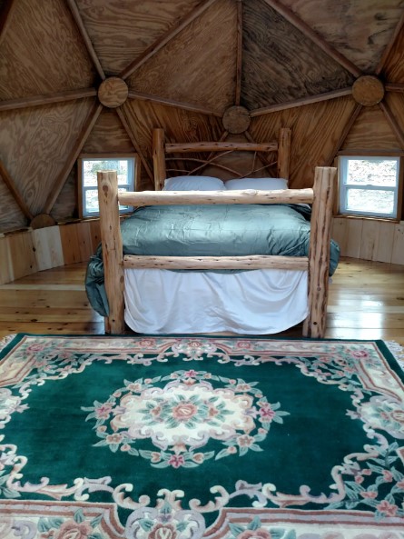 bed with wooden bed frame, patterned carpet and two windows around the bed