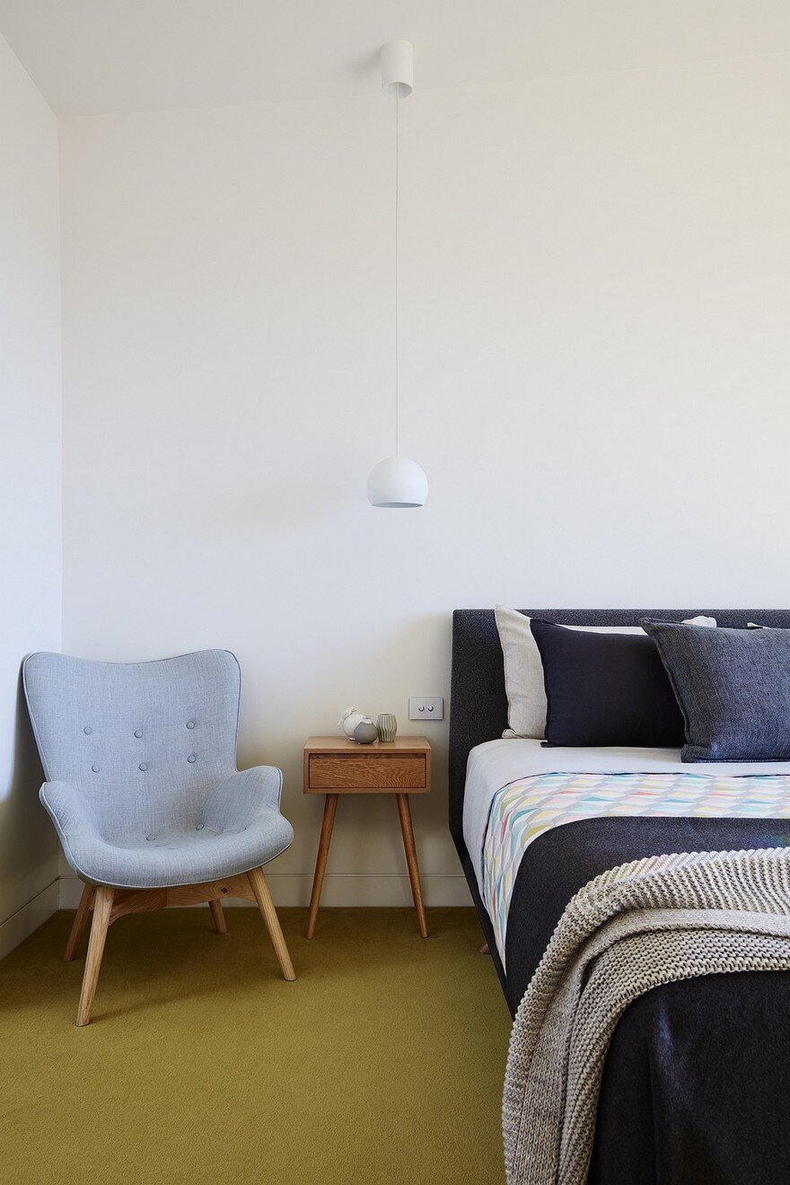 bedroom with a blue chair in the corner, wooden bedside table, low hanging lamp and a green carpet