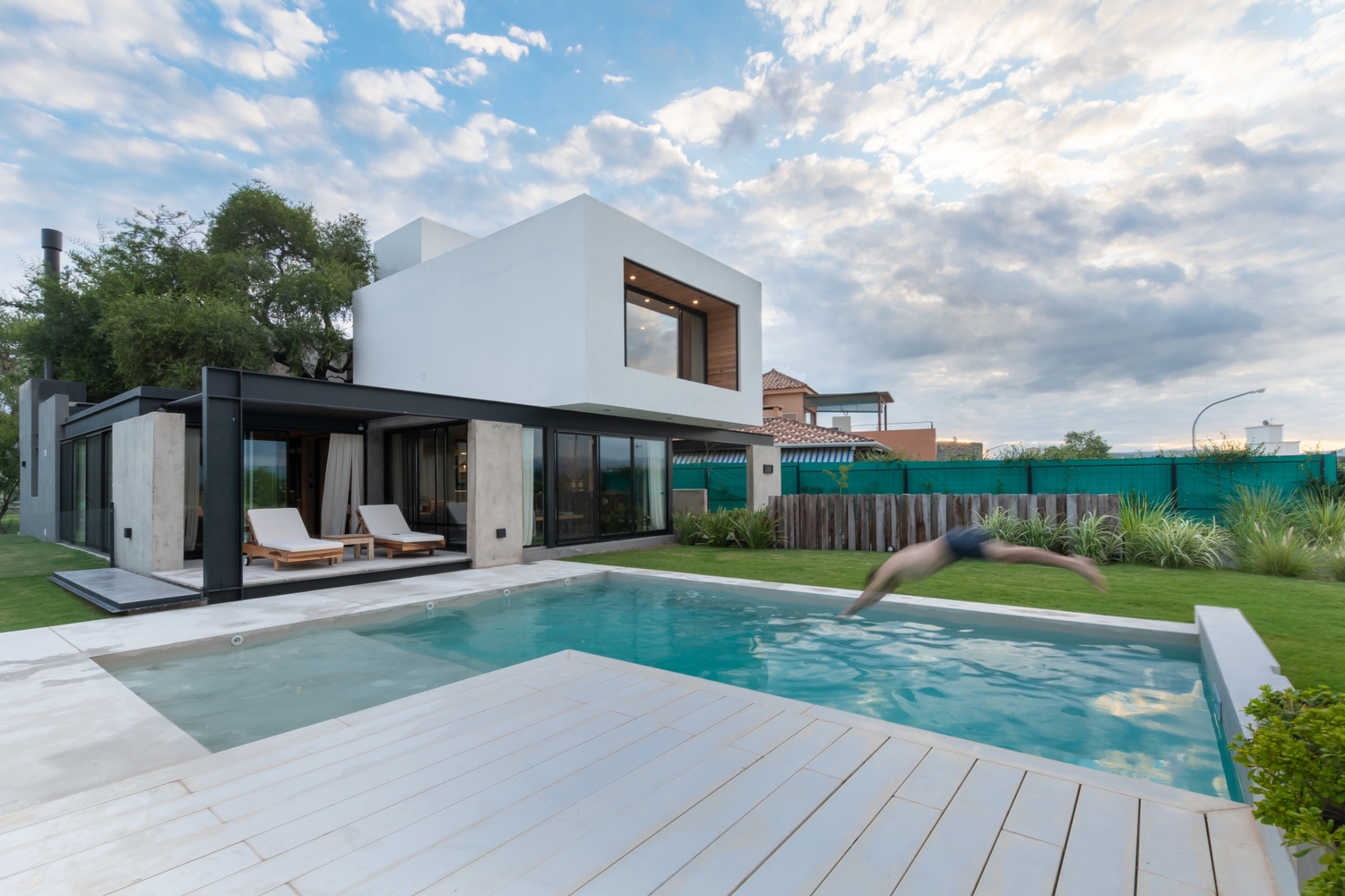 pool of a modern house surrounded by a lot of green land and deck chairs