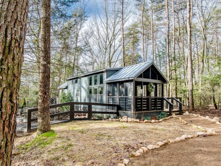 tiny house in woods with an exterior of wooden planks, a closed deck, and lots of porch space
