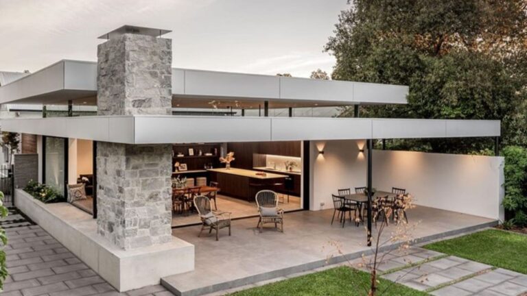exterior of modern mansion with flat roof, accent stone fireplace, alfresco, and a nice, green backyard surrounded by trees