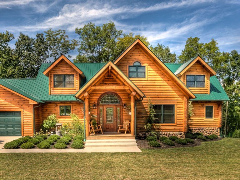 front side of the rustic log home the clear fork with orange-tint wood logs, a green roof, a garage, and greenery outside