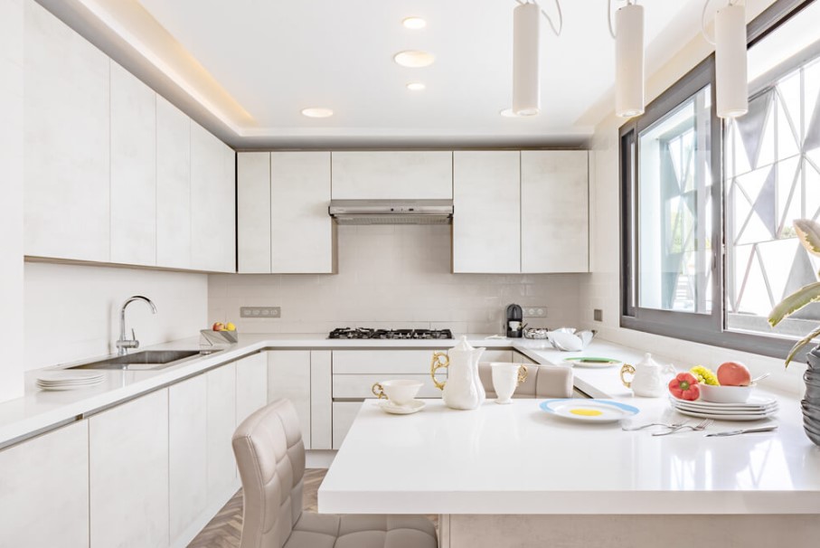 all white kitchen with white cabinets and a white countertop and big windows