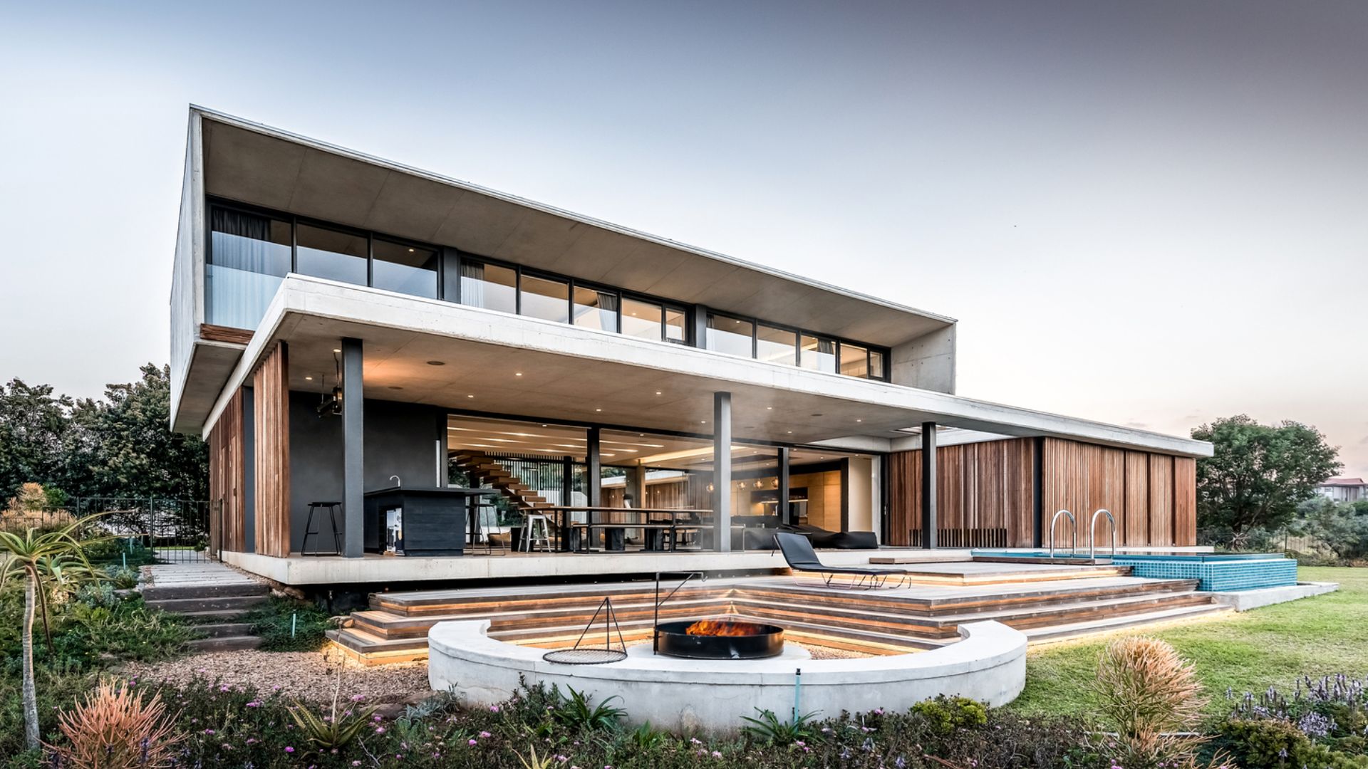 back side of the concrete house with wooden screens and a garden lounge area with a fire pit