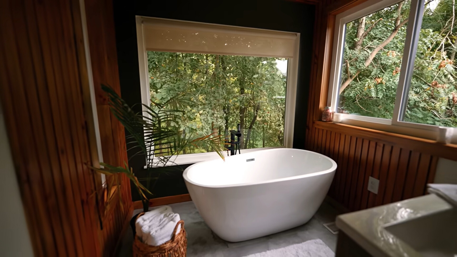 bathroom with a white bath tub and windows looking into the woods with a brown, wooden wall