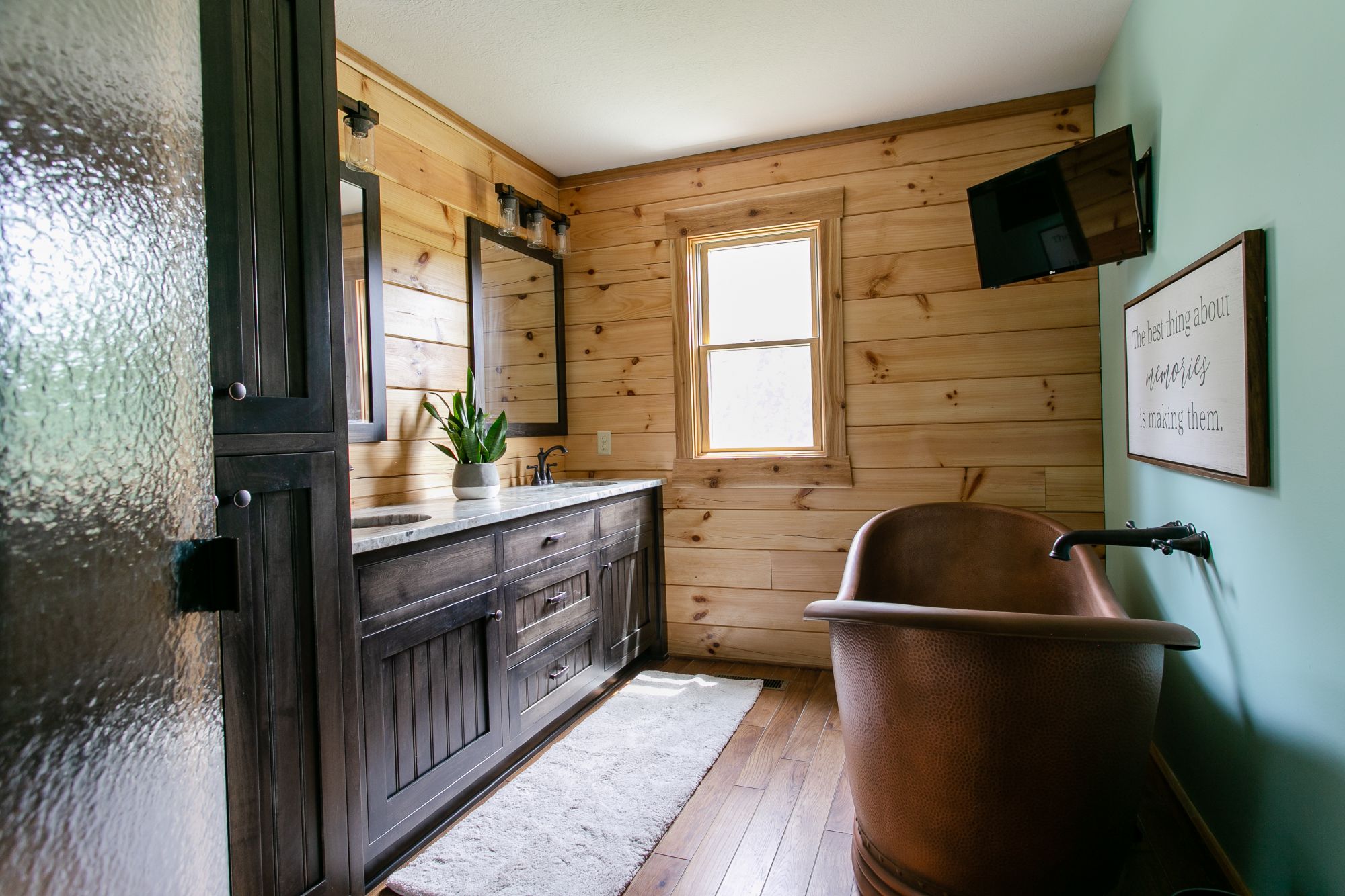 bathroom with a copper bathtub and a brown cabinet with two mirrors and two sinks