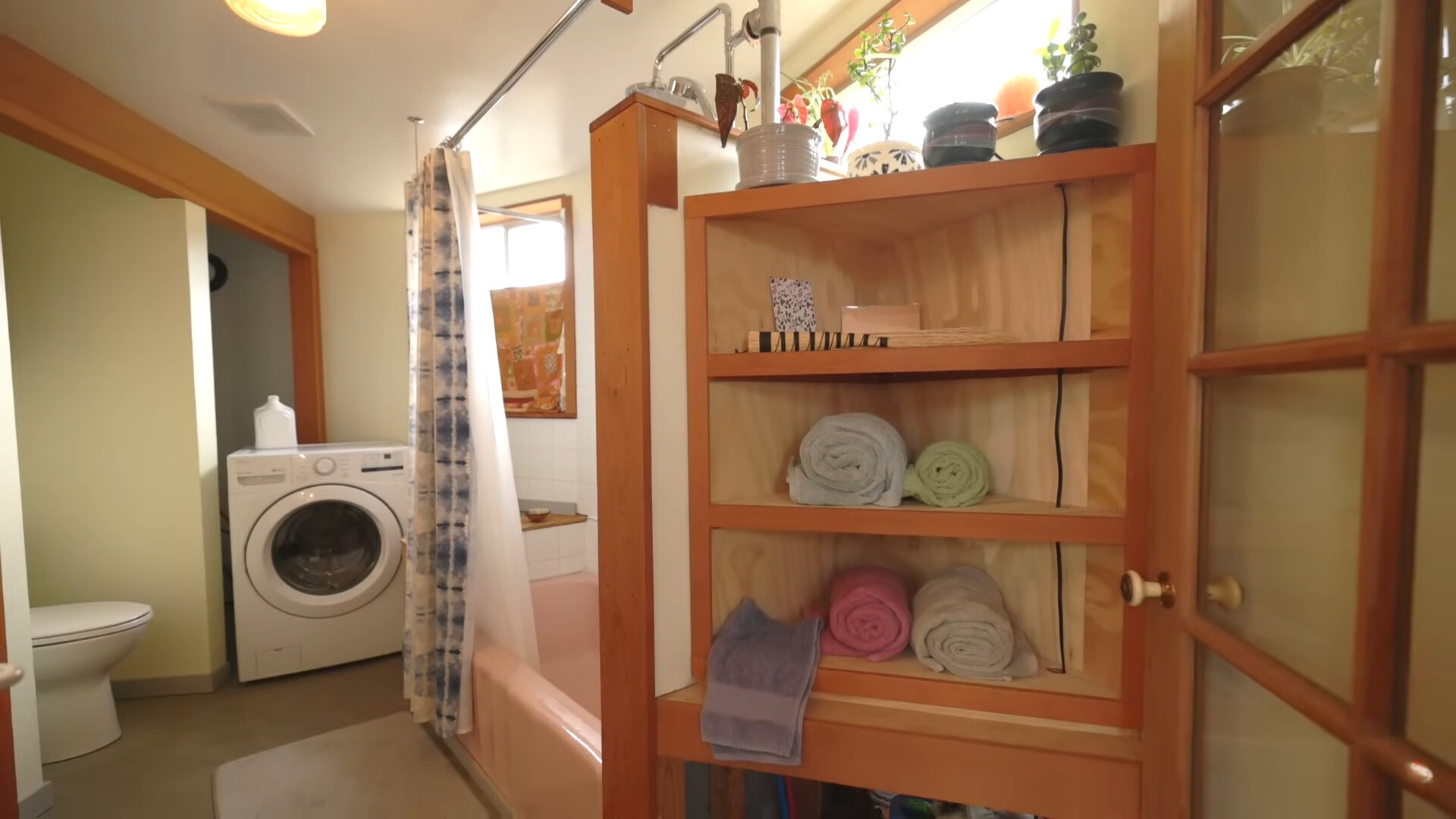 bathroom with a pink bathtub and a closet filled with towels