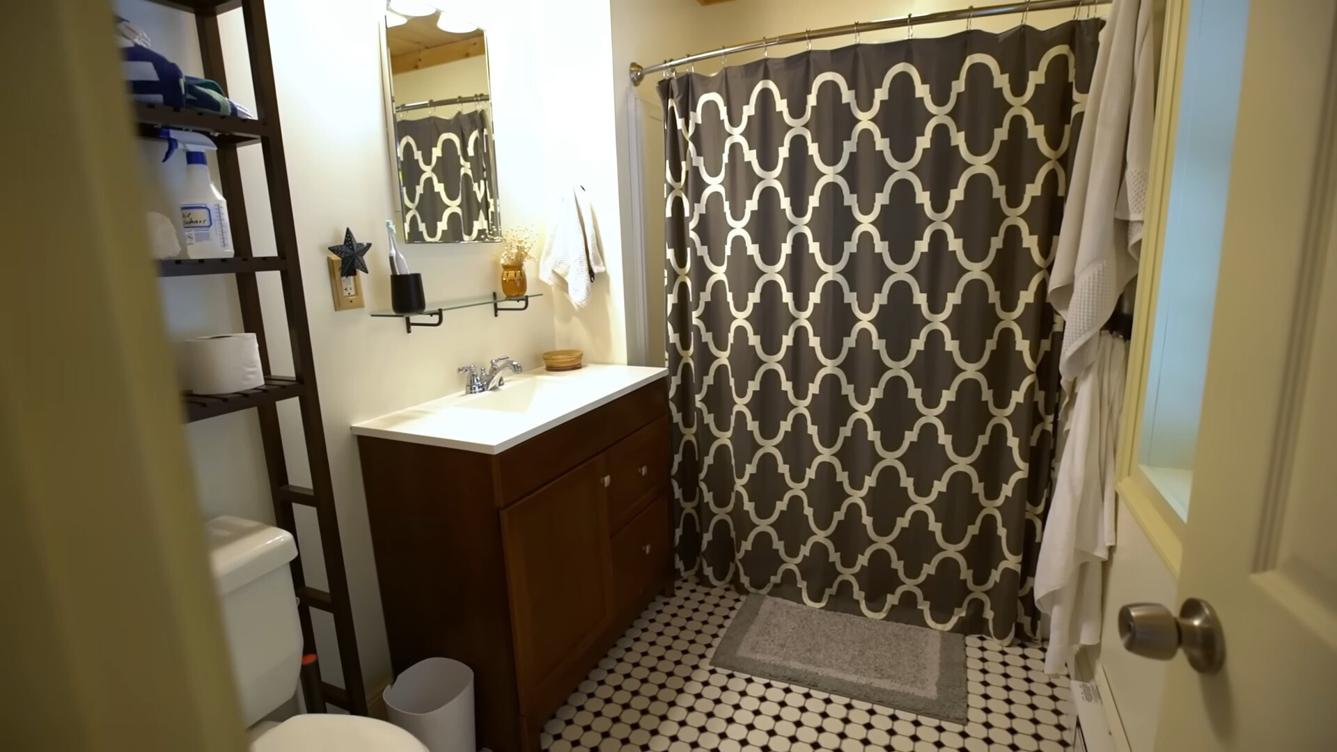 bathroom with a brown cabinet, white countertop, tall black shelf, small mirror and a shower with a textured black and white curtain