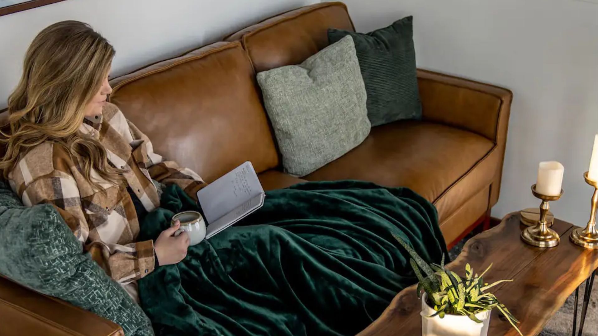 woman sitting on a beautiful brown leather couch with green pillows and a wooden coffee table