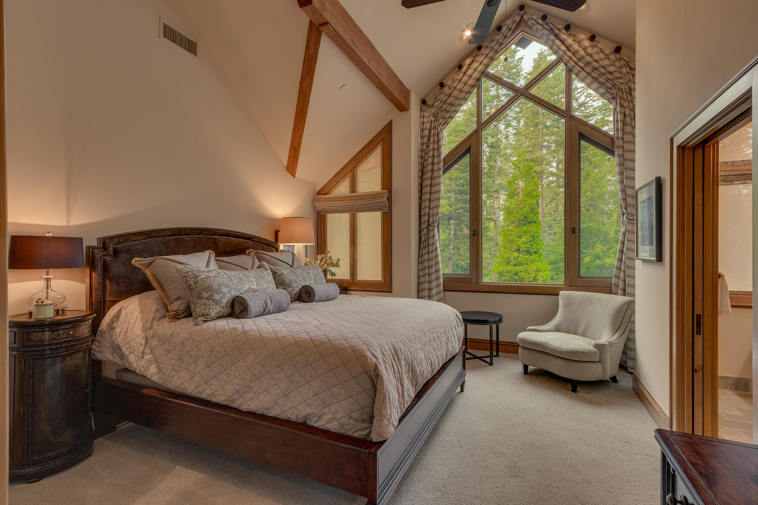 bedroom with view of the woods, comfortable bed and a chair in the corenr of the room