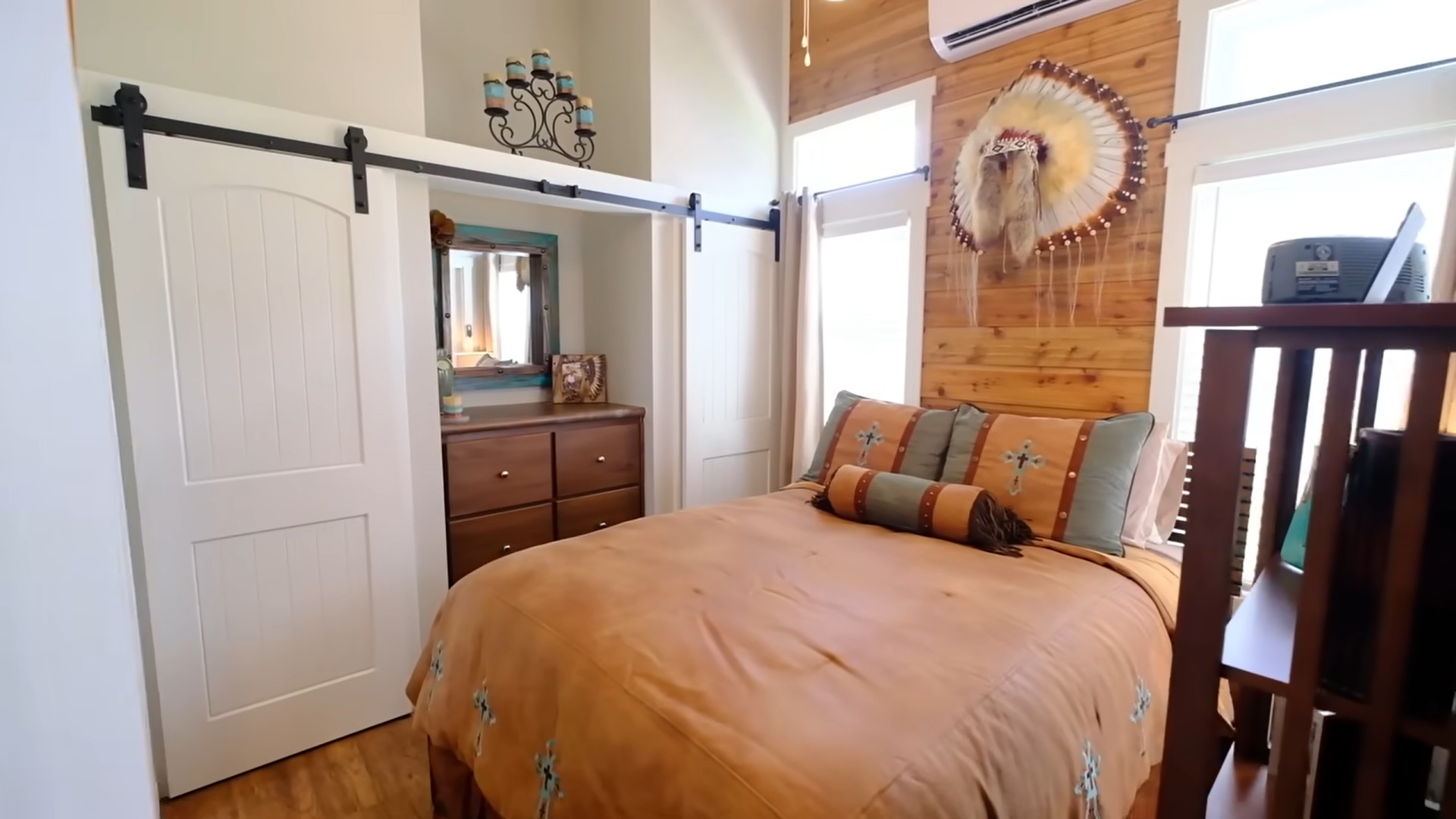 bedroom with one wooden wall, a bed in the middle, a brown cabinet and two closets hidden behind white doors