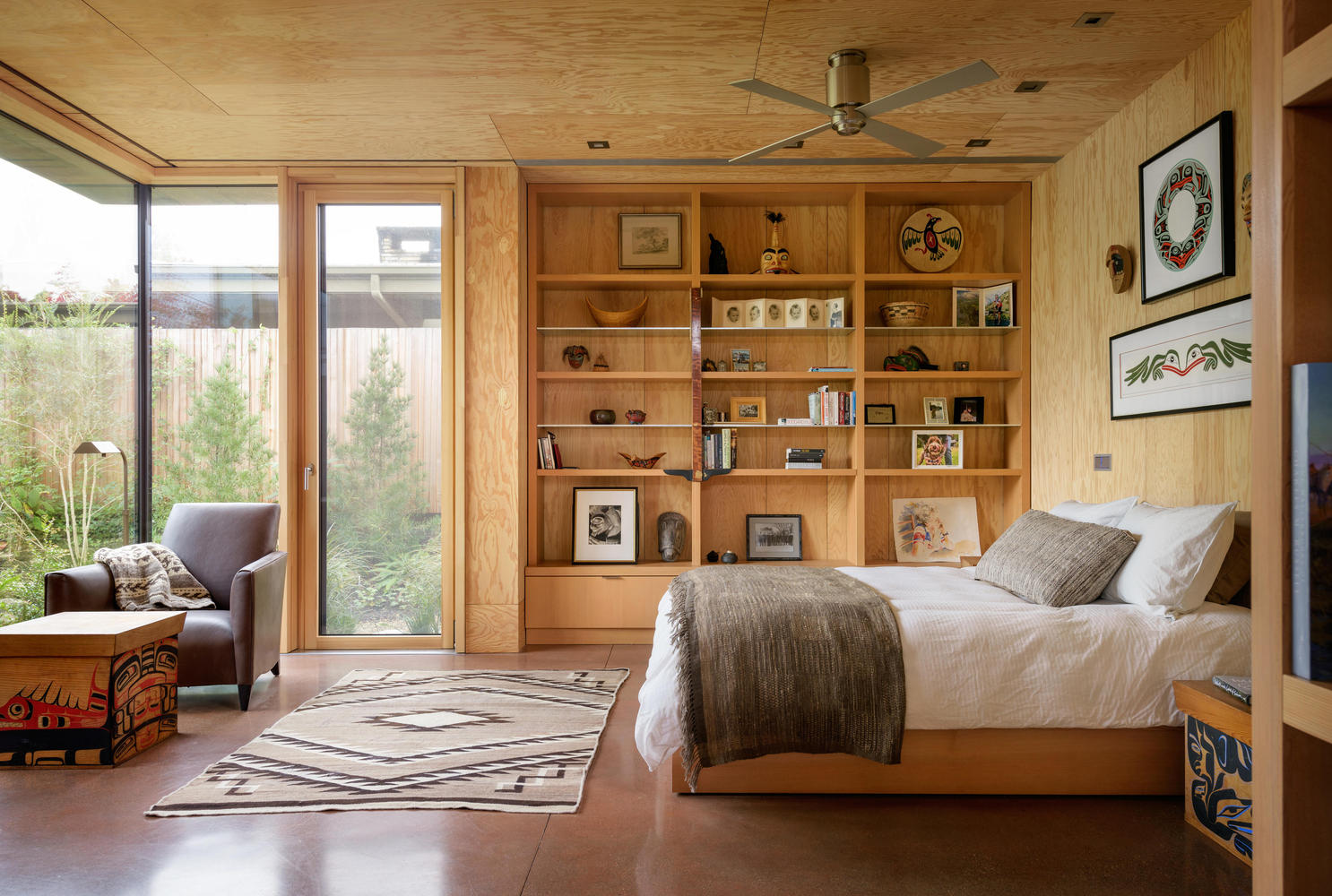 bedroom with floor to ceiling windows and a floor to ceiling shelf with decor and a sofa in the corner of the room