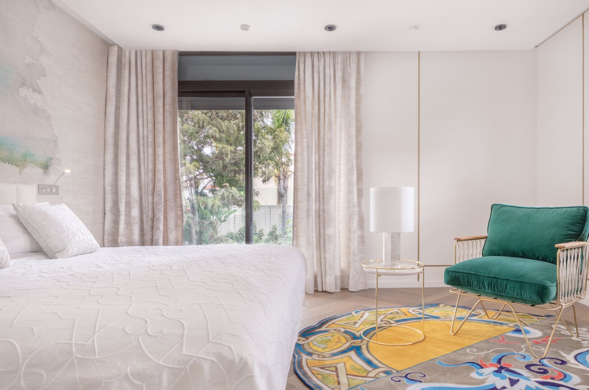 bedroom with a floor to ceiling window, big white bed, a green chair and a colorful carpet