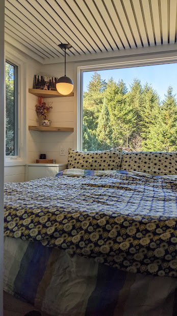 bedroom with a big window and textured bed sheets and shelves in the corner