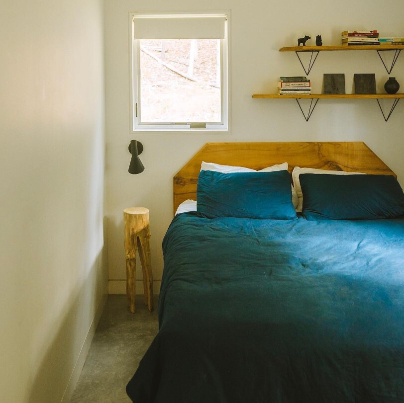 bedroom with a wooden bedside table, comfy bed, two shelves abive the bed and a window