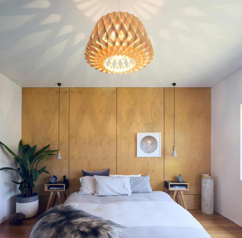 bedroom with a light brown wall, two low hanging lamps, a chandelier, two bedside tables on sides of the bed