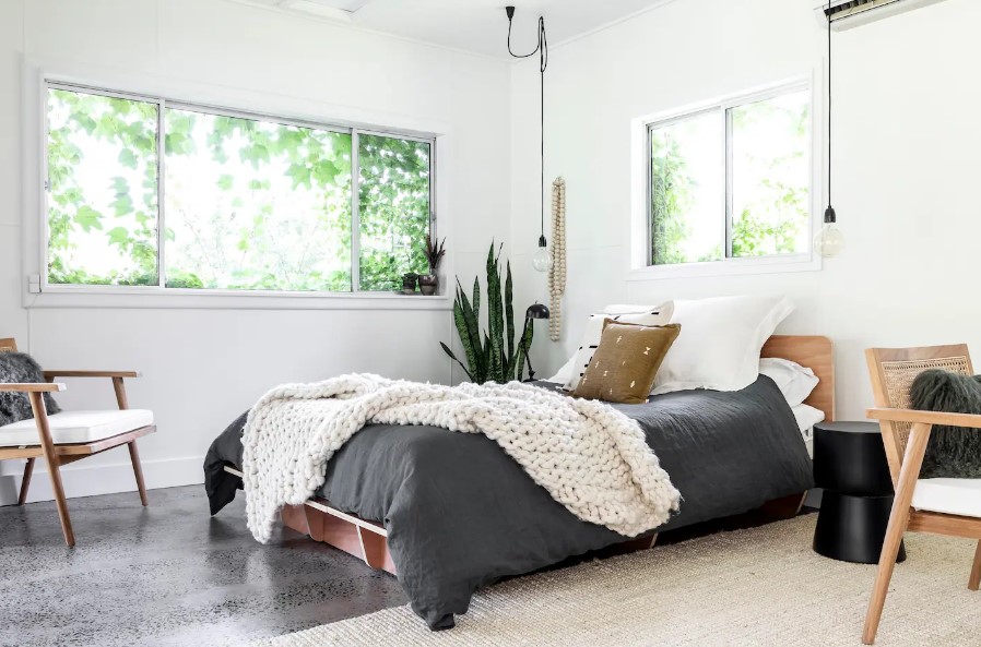 bedroom with a bed in the middle, white walls, windows around the room, low hanging lamps