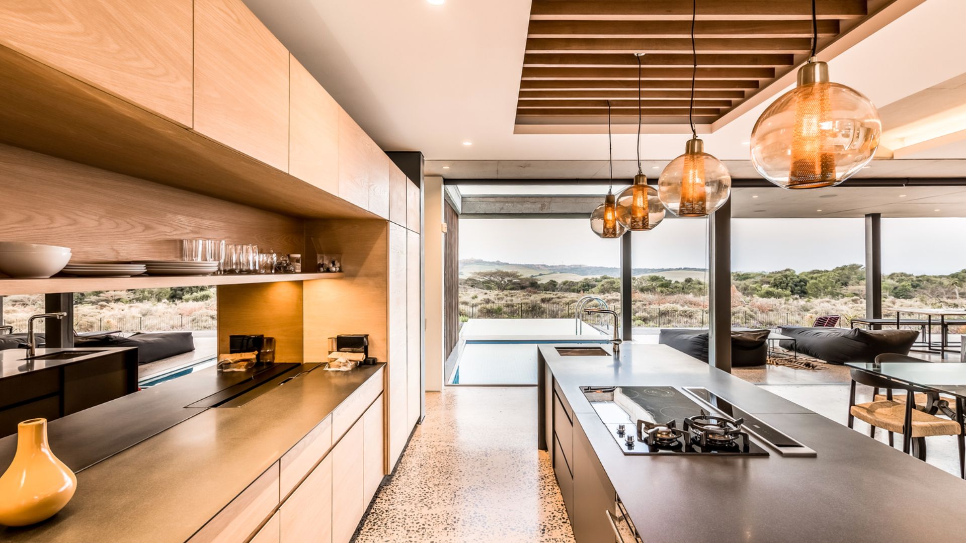 big kitchen with wooden cabinets and a gorgeous black backsplash wall with an island in black and golden lights above it