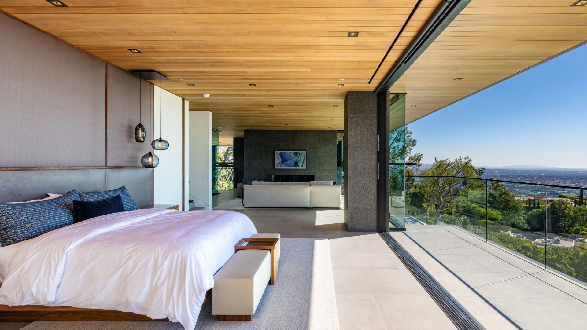 view from master bedroom with a big, comfortable bed and plenty of natural light coming from the glass wall