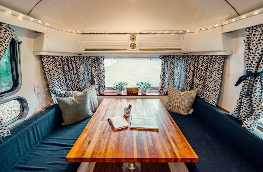 living area of a camper with blue couches, brown dining table and windows all around it