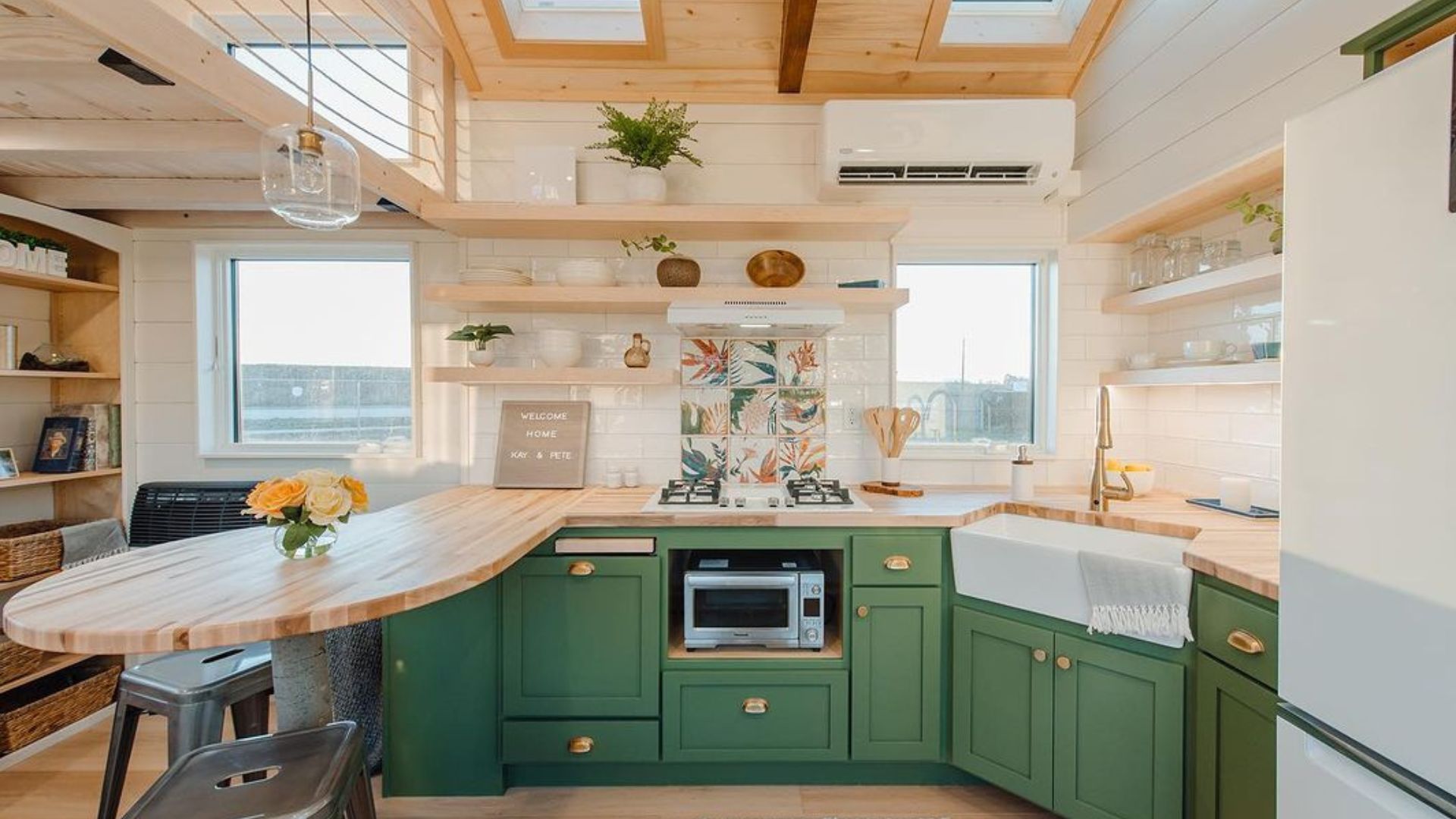 bright kitchen with green cabinets, floating shelves, a fridge, a small over, and a round dining area