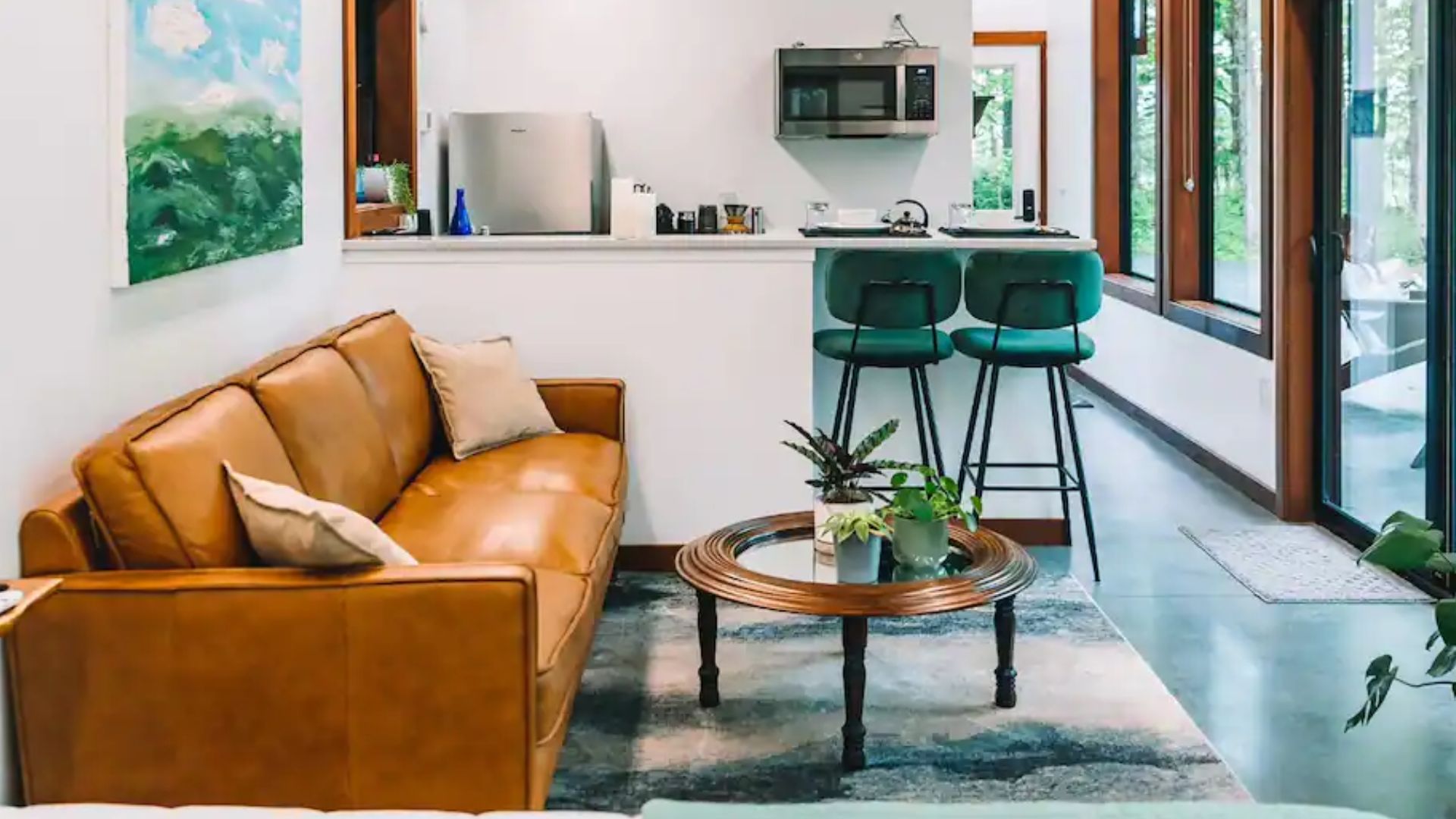 pretty brown couch with a round mirror coffee table and two green bar chairs in the dining area