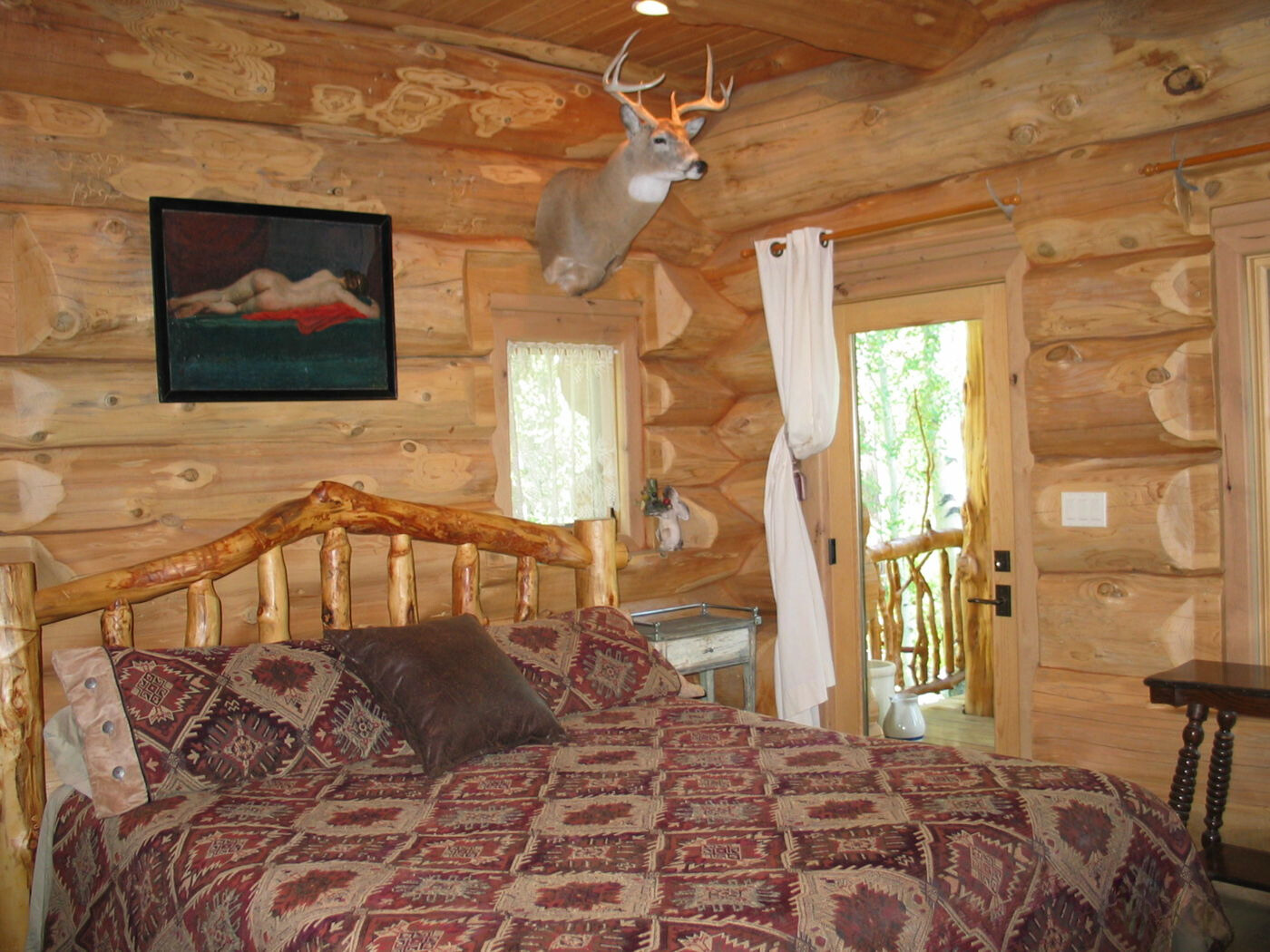 cabin bedroom with brown, wooden walls, deer head as decor, textured red bed sheets and a balcony with glass door