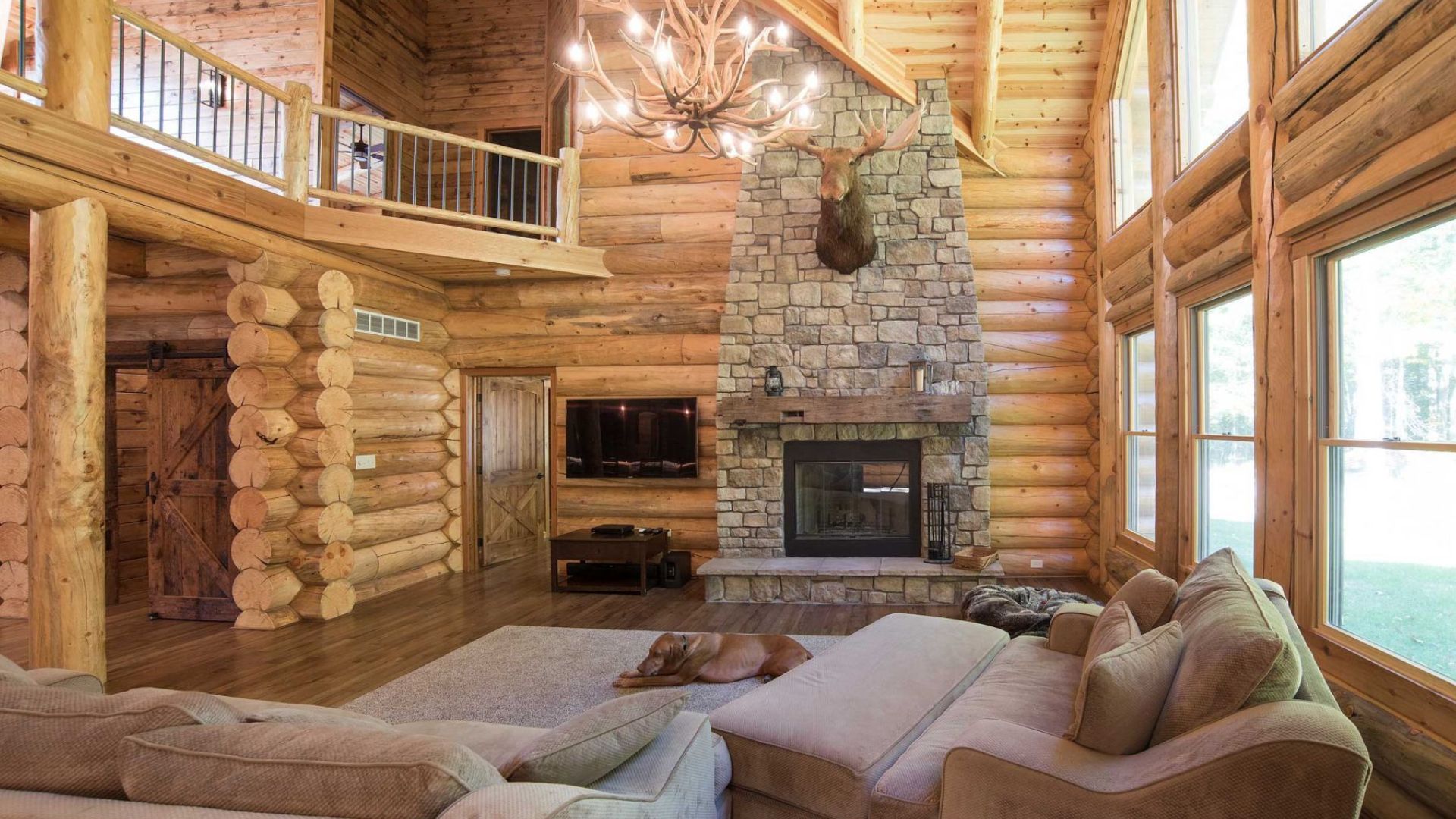 living room with comfy sofas, a huge stone direplace and unusual antlers chandelier