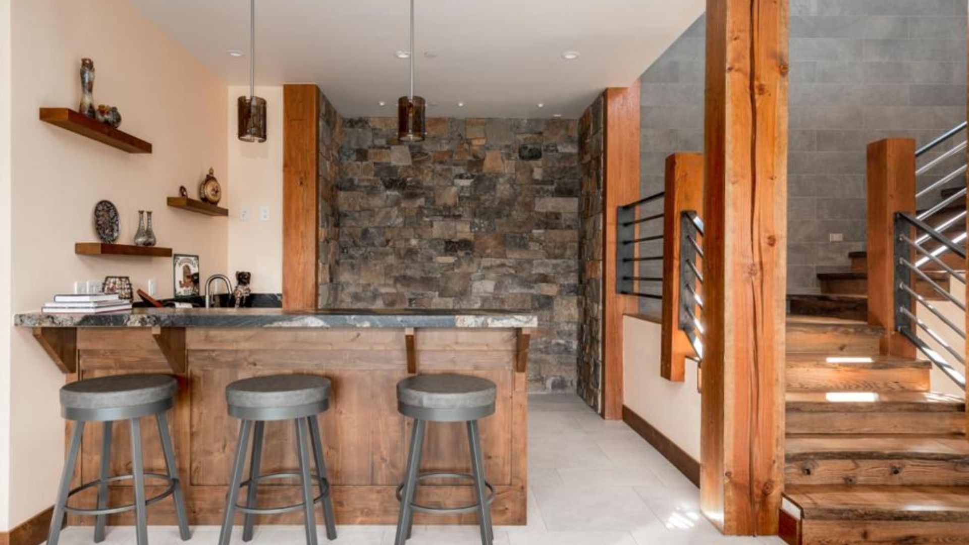 downstairs bar area with wood and stone details, three bar stools and a wide staircase