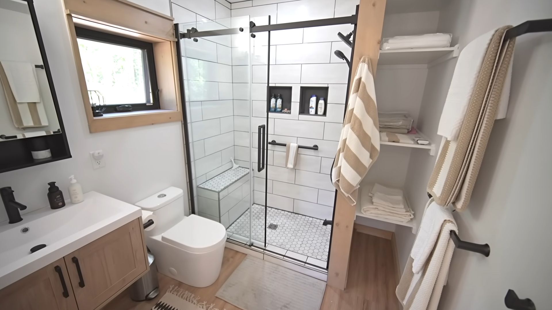 master bathroom with a walk-in shower, white tiles, black hardware, and plenty of storage space