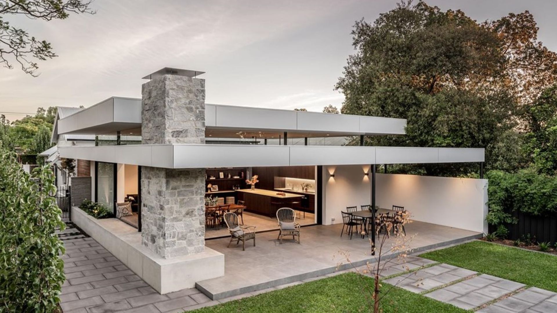 exterior of modern mansion with flat roof, accent stone fireplace, alfresco, and a nice, green backyard surrounded by trees