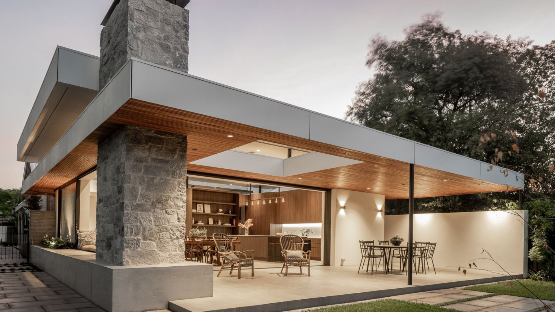 exterior of modern house with lights on, a dominant fireplace, and an alfresco area