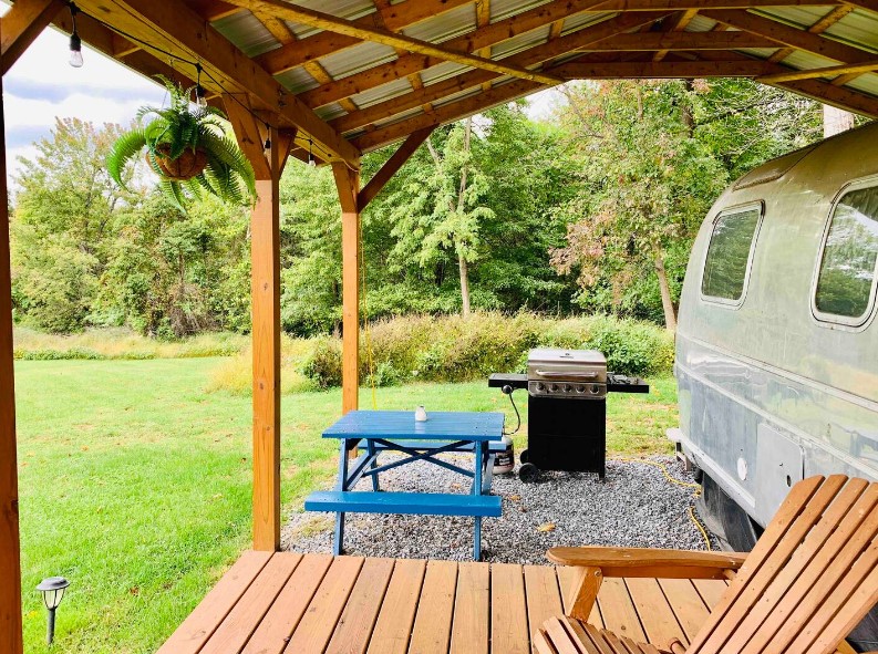 a gril and a blue dining table with blue chairs outside of a camper