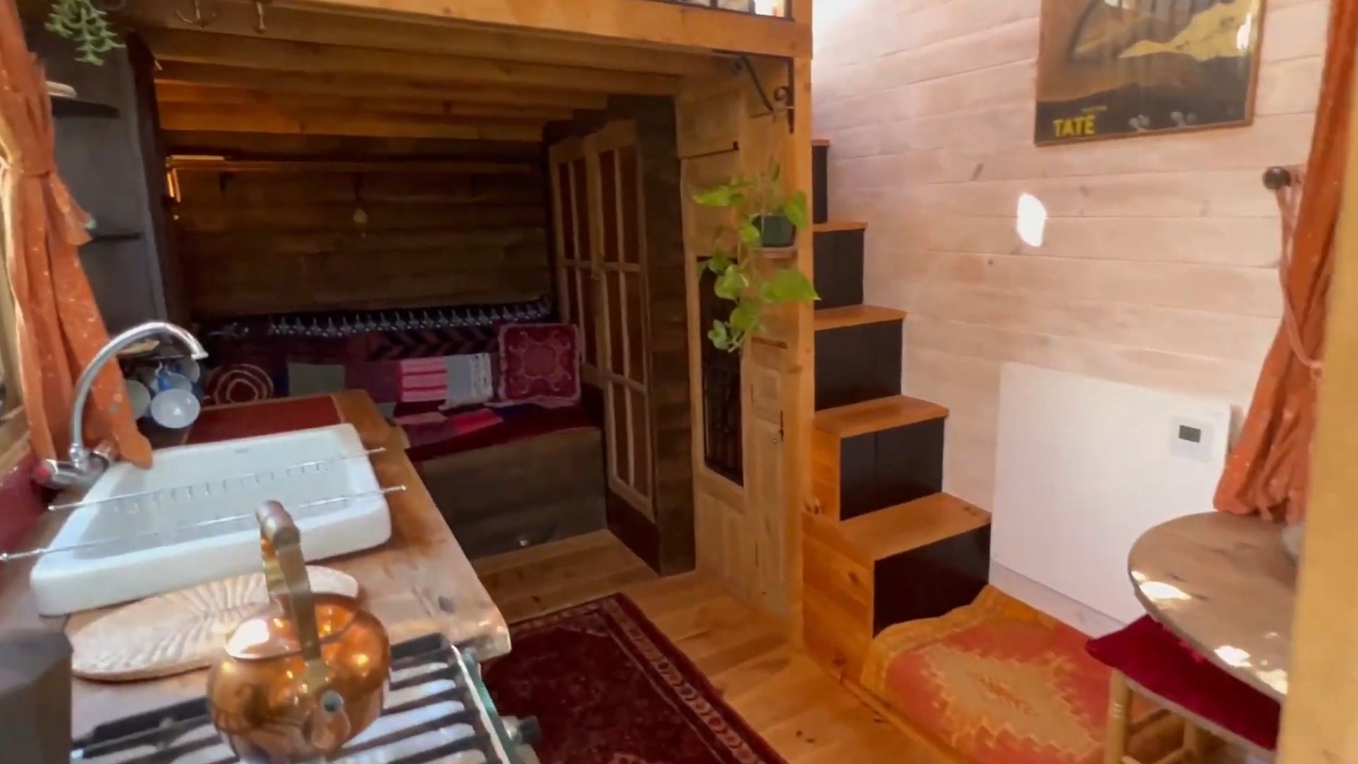 inside the tiny house, kitchen area on the left with a big, white sink, living room in the back with a tiny sofa, and block stairs that lead upstairs to the loft