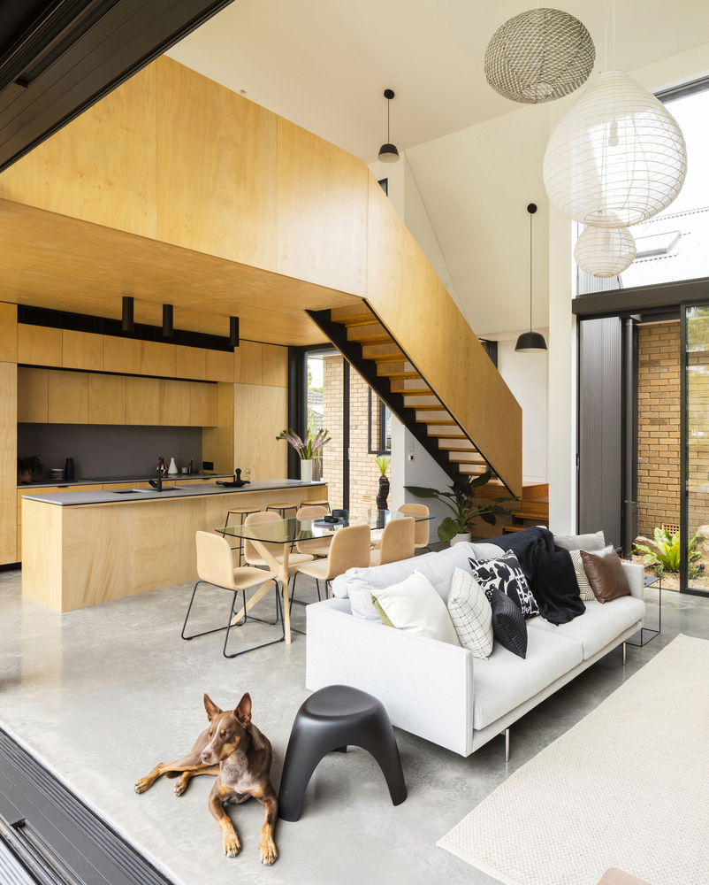 kitchen of a modern house with brown cabinets, light gray countertop, glass dining table surrounded by chairs