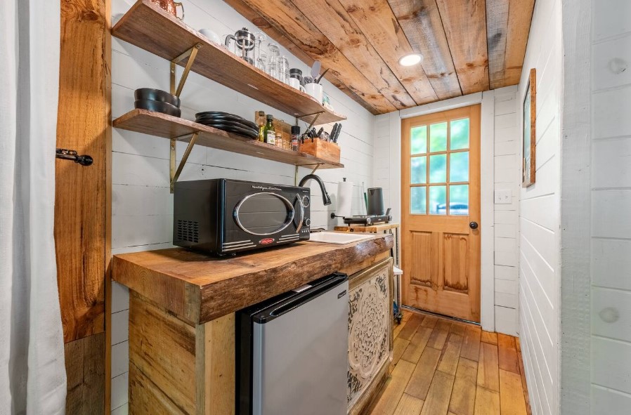 kitchen with a wooden countertop, black microwave and a white sink and wooden shelves