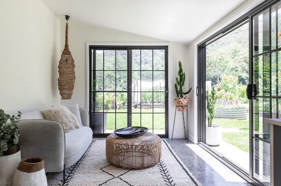 living room with a white walls, plants, gray couch, small round table and glass doors,