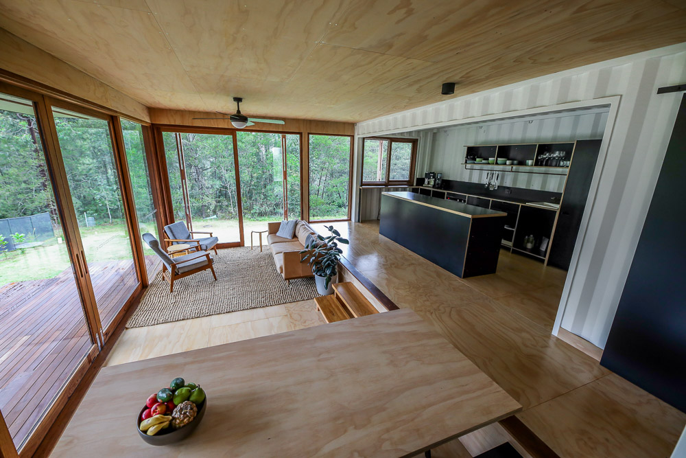 open space of a living room with a couch and two chairs, dining room with a brown dining table and a kitchen with black cabinets