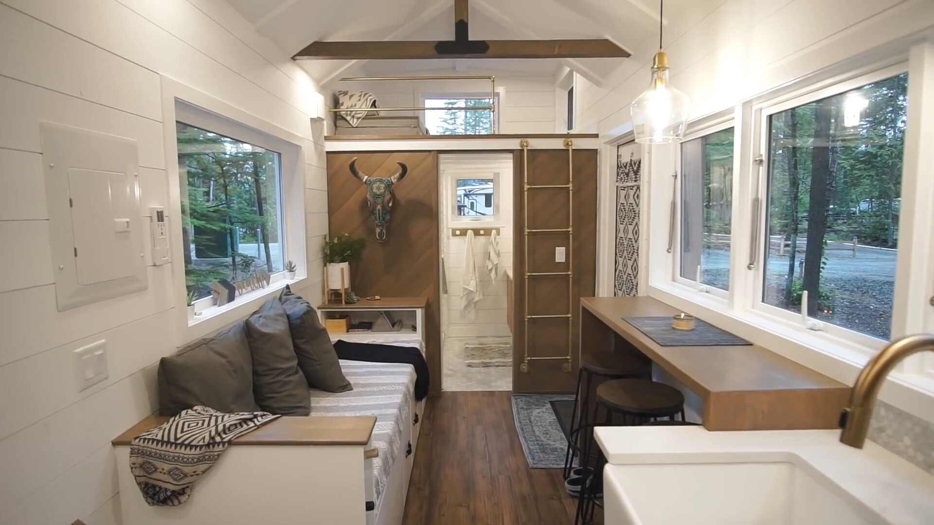 living room with a big couch, brown desk, two black chairs and big windows on both sides of the container